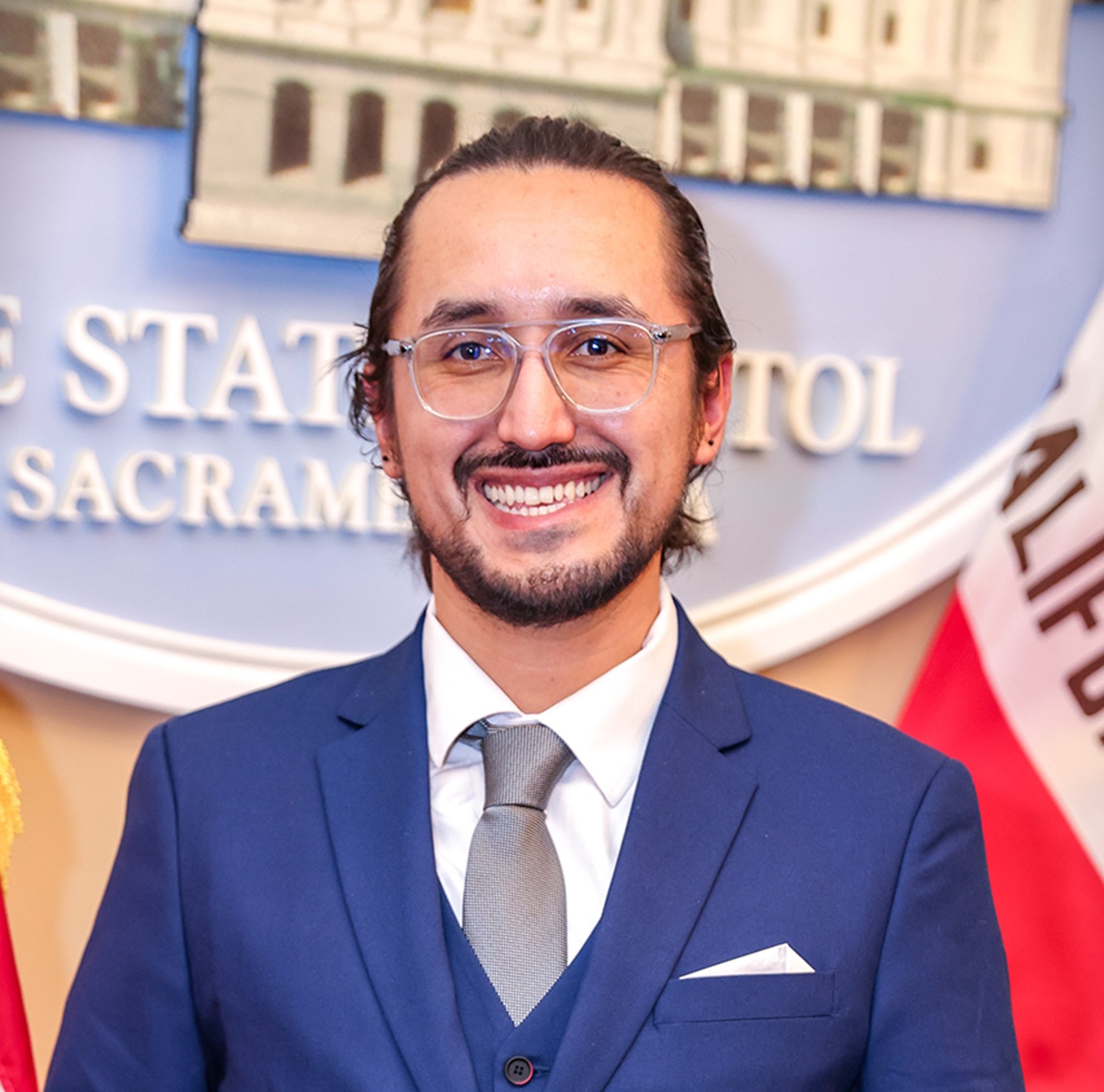 Cristian smiling at camera with blue suit and glasses on.
