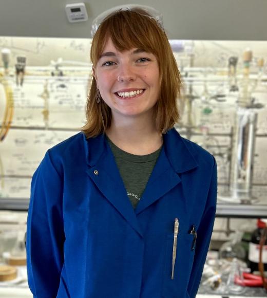 Anna Vernier is standing in a lab with a blue lab coat on and smiling. 