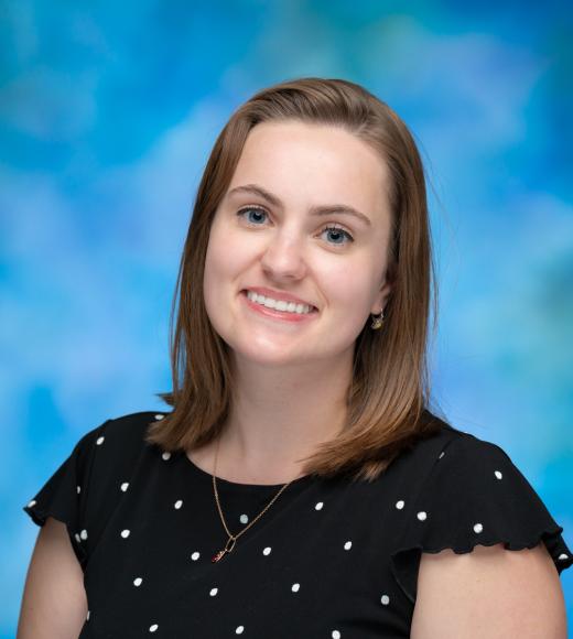 Nicole Keough is smiling in front of a blue background wearing a polkadot shirt.