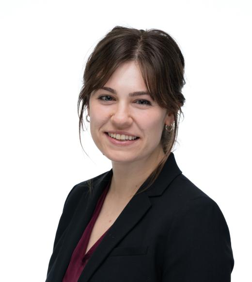 Eleanor Pressman is facing the camera smiling in front of a white background while wearing a black blazer.