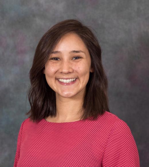 Nicole is smiling wearing a pink long sleeve shirt in front of a gray background.