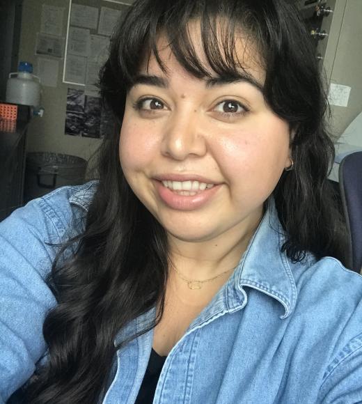 Rachel is inside a room wearing a jean textured long sleeve shirt while smiling at the camera.