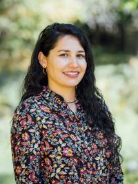 Alejandra is standing outside smiling at the camera with a black and floral blouse on.