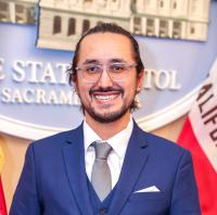 Cristian smiling at camera with blue suit and glasses on.