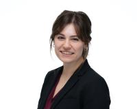 Eleanor Pressman is facing the camera smiling in front of a white background while wearing a black blazer.