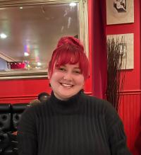 Nathalie is smiling at the camera in black shirt inside a red room.