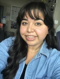 Rachel is inside a room wearing a jean textured long sleeve shirt while smiling at the camera.