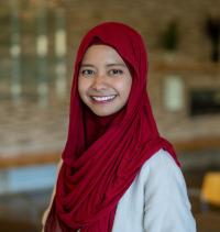Davrina is smiling at the camera with a red hijab and a white shirt.
