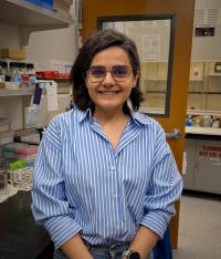 Sara smiling at the camera in a blue and white striped shirt while sitting in the lab.